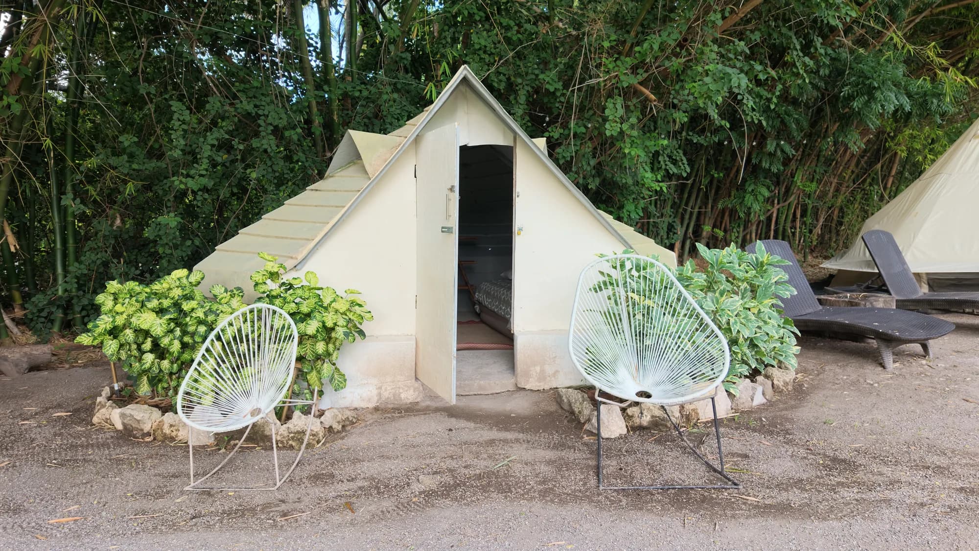 Tienda de glamping estilo cabaña de lona con sillas Acapulco a la entrada, entre bambú